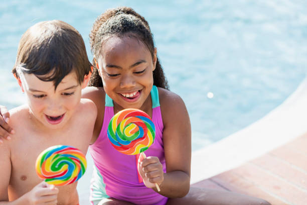 istock Two multi-ethnic children sitting by pool with lollipops 1128250968