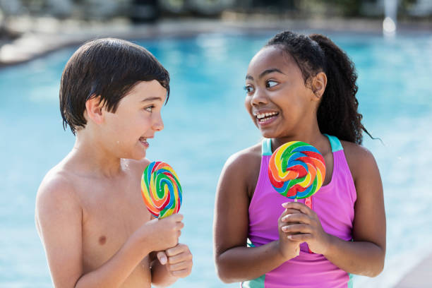 istock Two multi-ethnic children sitting by pool with lollipops 1128250971