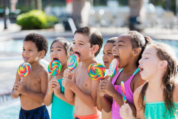 istock Multi-ethnic children licking lollipops by swimming pool 1128251502