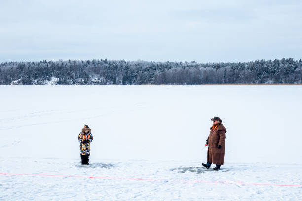 vista del paesaggio invernale di un uomo e di un bambino su una pesca ghiacciata sul ghiaccio del lago. - sweden fishing child little boys foto e immagini stock