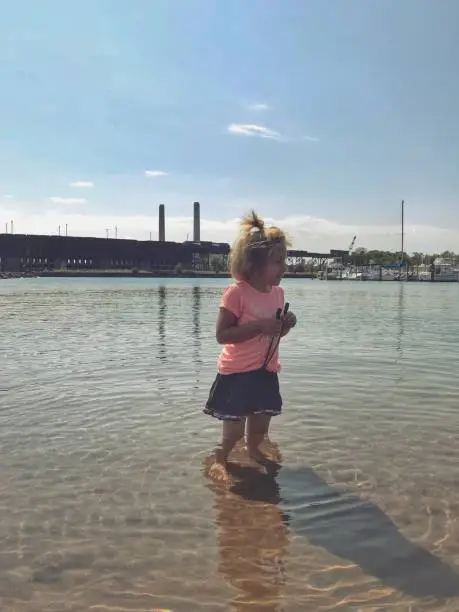 Photo of Playing in Lake Superior, Marquette, Michigan , one small child making ripples in the water with smokestacks and train in background .