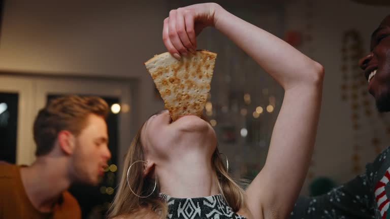 Handheld shot of teenage boys and girl eating delicious pizza in party. Happy male and female friends are enjoying fast food. They are celebrating Christmas at home.