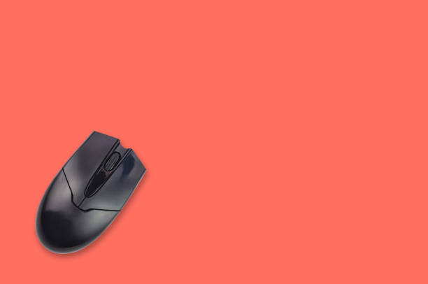 istock Single black plastic optical computer mouse on office table living coral color. Top view. Copy space for your text. Business or education concept 1128259223