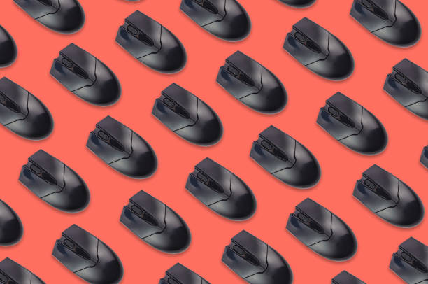 istock Rows of black plastic optical computer mouses on office table living coral color. Top view 1128259256