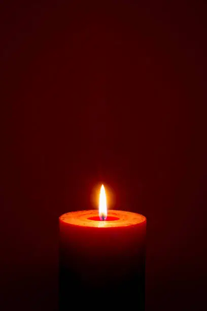 Photo of burning candle on dark red background