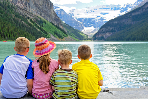 Rear view of four children sitting together on the edge of beautiful Lake Louise.