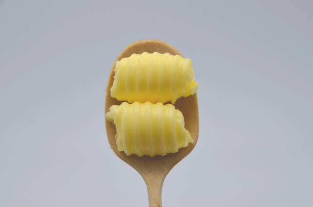roll of butter on a wooden spoon. Butter is used for cooking and baking and it adds a tasty flavor to the food. Picture is ideal for advertising dairy products,