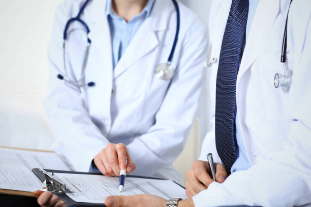 istock Two unknown doctors filling up medical form on clipboard, just hands closeup. Physicians asking question to patient or discussing medication program. Healthcare, insurance and medicine concept. 1128280291