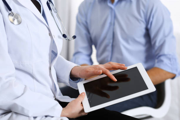 istock Female doctor using  touchpad or tablet computer while consulting man patient in hospital. Medicine and healthcare concept. 1128280303
