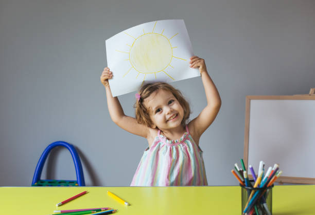 child drawing at home Happy little girl holding drawing of a sun at home coloring photos stock pictures, royalty-free photos & images