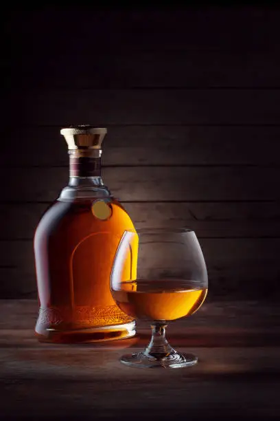 view of glass of  whiskey and a bottle aside on color wooden  background.