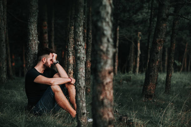 istock Young depressed man sitting alone in the forest 1128287650