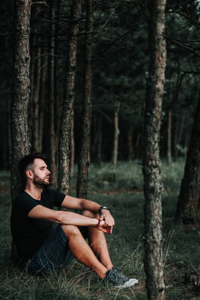 istock Young depressed man sitting alone in the forest 1128287653