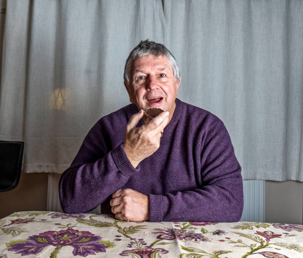 Senior Caucasian man eating chocolate biscuit in living room