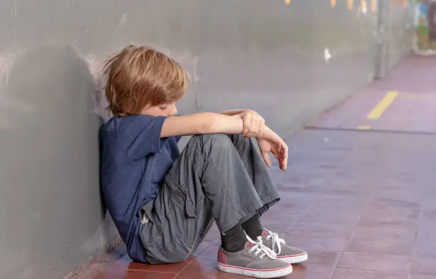 Photo of Elementary School. Sad little boy oppressing in the schoolyard. Bullying concept