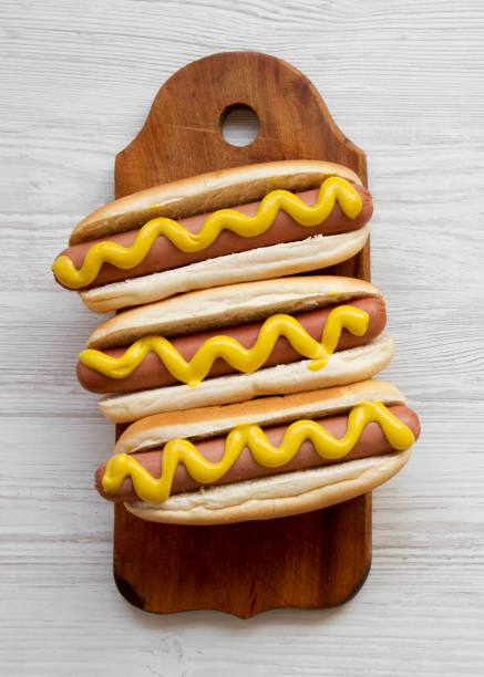 istock Hotdog with yellow mustard on rustic board on white wooden surface, top view. Flat lay, overhead, from above. 1128308553