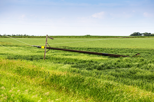 A broken and fallen electrical power pole in a rural field after a storm.