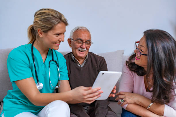 istock Elder married couple sitting on the couch and smiling at nurse with a tablet computer 1128312894