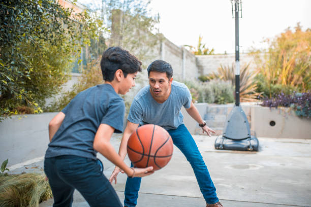 vater und sohn mit armen angehoben basketball spielen - basketball basketball hoop california southern california stock-fotos und bilder