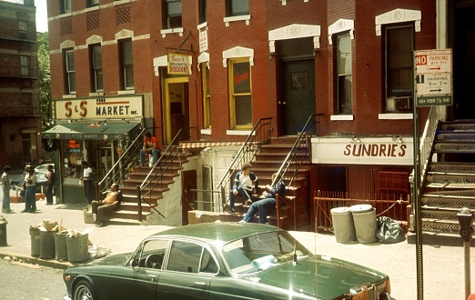 New York City, NY, USA, 1980. Street Scene in a New York City District (Bronx, Brooklyn ...). Also: Residents, buildings, shops and a parked cars.