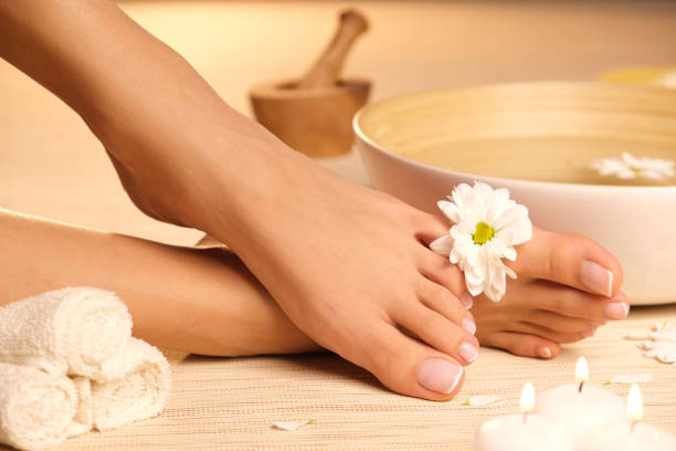 The picture of ideal done manicure and pedicure. Female hands and legs in the spa spot. Female hands and legs in the spa spot in nice, cozy place with camomile flowers. foot spa treatment stock pictures, royalty-free photos & images