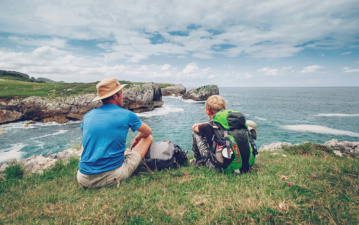 Father and son backpackers rest on the rocky sea side