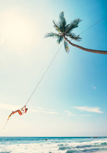 istock Woman dangles on tropical palm tree swing over ocean waves 1128322254