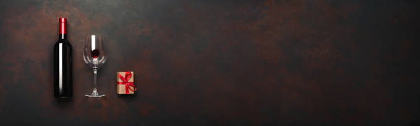 Bottle of wine with wineglass and gift box on rusty brown background. Panoramic top view with space for your text