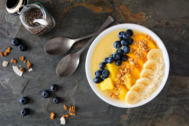 istock Pineapple, mango smoothie bowl with coconut, bananas, blueberries and granola, above view table scene on slate 1128328073