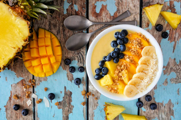 istock Pineapple, mango smoothie bowl with coconut, bananas, blueberries and granola, top view table scene on wood 1128328171