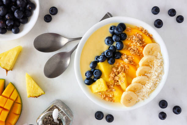 istock Pineapple, mango smoothie bowl with coconut, bananas, blueberries and granola, top view on a bright background 1128328274