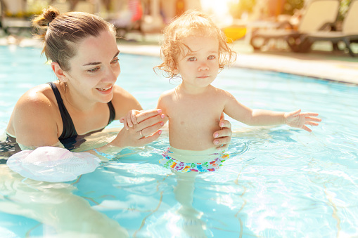 Mom and little daughter are played in the open swimming pool. Family with one child on vacation in warm countries. Positive people on vacation. Summer leisure