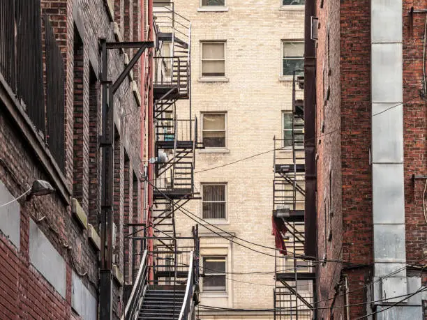 Photo of Fire escape stairs and ladder, in metal, on a typical North American old brick building from the Old Montreal, Quebec, Canada. These stairs, made for emergency, are symbolic of the American architecture