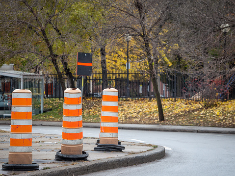 Picture of various construction barrels abiding by North American road regulations, on display on a construction site in the center of Montreal, Quebec, Canada. Construction barrels, or drums, are traffic control devices used to channel motor vehicle traffic through construction sites or to warn motorists of construction activity near the roadway.