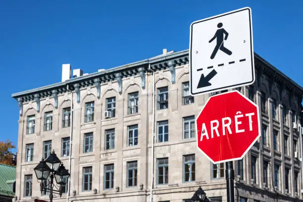 Picture of a Quebec stop sign, translated in French, called according to Quebec French speaking regulations panneau d'arret, next to a roadisgn indicating the presence of a pedestrian crossing nearby