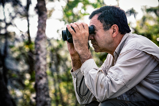 Hispanic mature man looking through binoculars in the forest