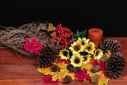 Silk maple leaves, beautiful bouquet of sunflowers, frosted pine cones and orange candle on tabletop with dark background. Thanksgiving, Halloween, Holiday, Festive,