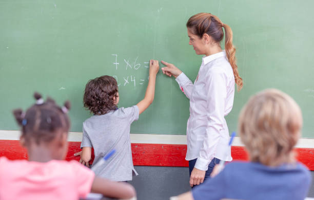 istock Elementary School. Smiling teacher teaching math to schoolboy at blackboard. Teaching concept 1128389733
