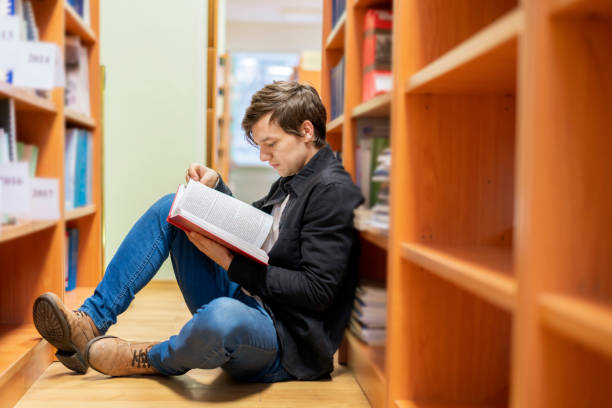 istock man in library reading book sitting under the book shelf b 1128391457