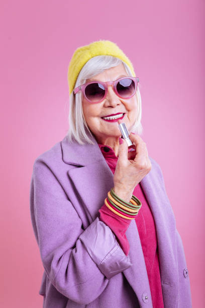 istock Cheerful elderly lady wearing purple coat smiling coloring lips 1128391655