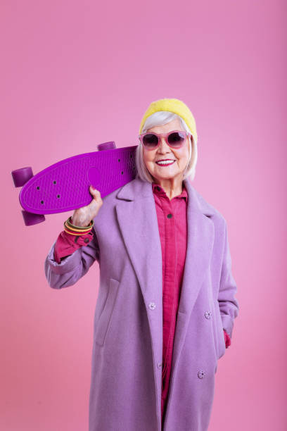 istock Modern beaming retired lady holding bright purple skateboard 1128391661