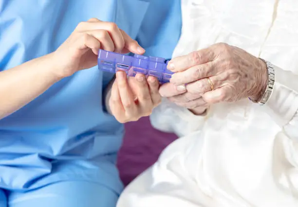 Photo of Nurse giving a weekly container of tablets to the elderly woman patient