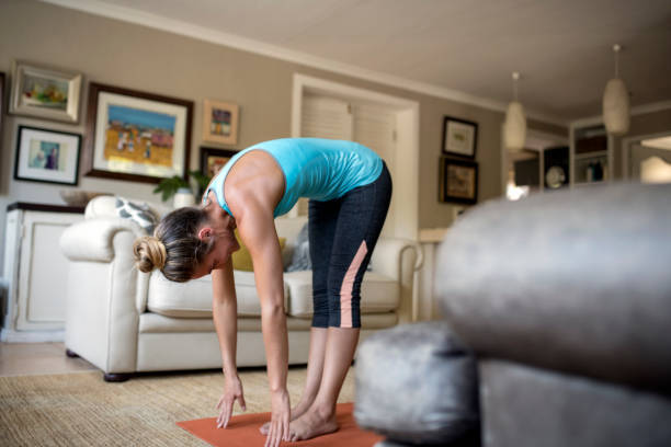 Full length of woman bending forward while practicing yoga. Young female is exercising in living room. She is training at home.
