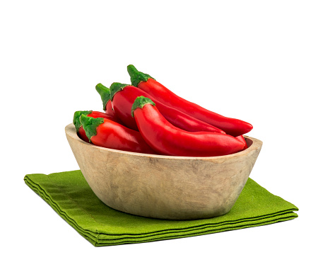 Red pepper in wooden bowl and green table napkin isolated on the white background.