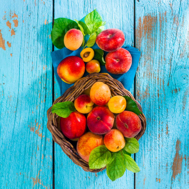 frutas de verano en cesta de mimbre sobre madera vieja azul - peach nectarine portion fruit fotografías e imágenes de stock