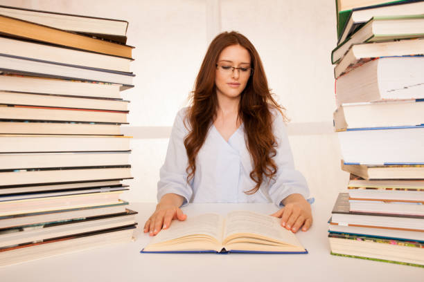 istock attractive young woman studies wtih hugr book piles on her desk 1128397728