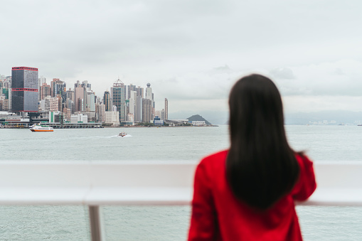 Woman standing by bay, looking out at city across water, focus on buildings, architecture