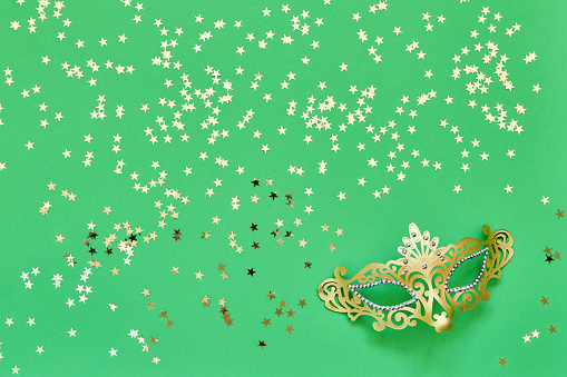 Golden carnival mask and golden stars on green background. Top view, copy space. Carnival party celebration concept.