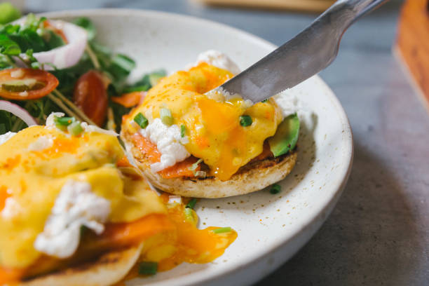istock Close up Eggs Benedict with salmon and avocado cut by knife, Served with salad in white plate. 1128409434