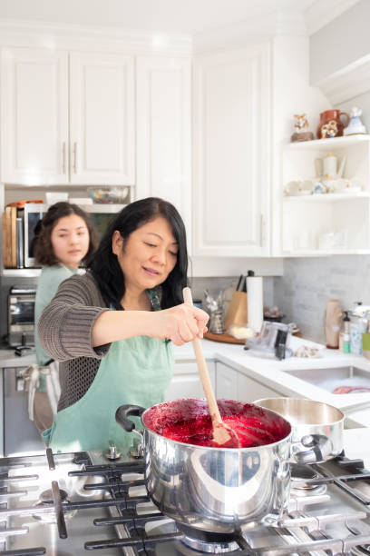 Asian Mother and Multi-Ethnic Daughter Making Jam in Home Kitchen